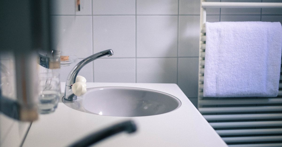 Een witte wastafel in de badkamer met een chromen kraan en een handdoek ernaast.
