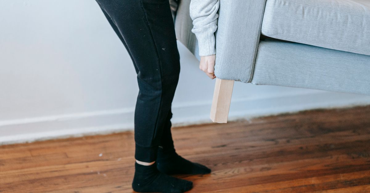 Iemand tilt een bank op om er een houten blok onder te plaatsen ter bescherming van de houten vloer.