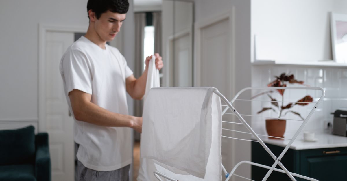 Een man hangt een wit wasgoed op een droogrek in een woonkamer.