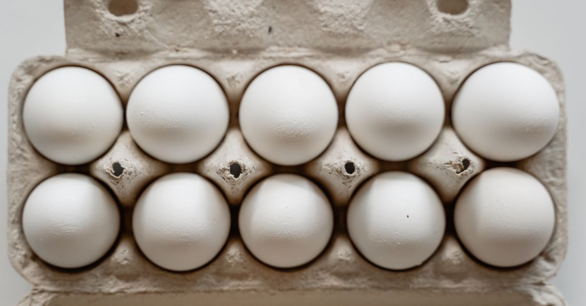 Een kartonnen eierdoos met tien witte eieren, van bovenaf gefotografeerd.