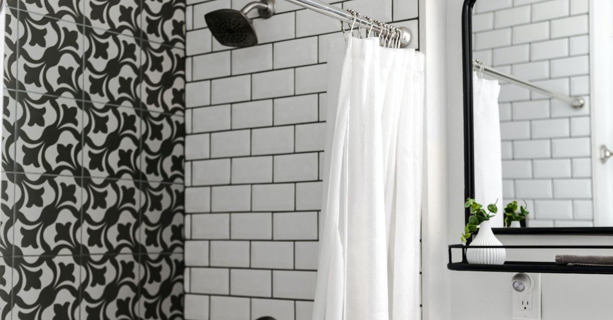 Witte badkamer met subway tegels, glazen douchewand met chromen douchekop en een witte douchegordijn.