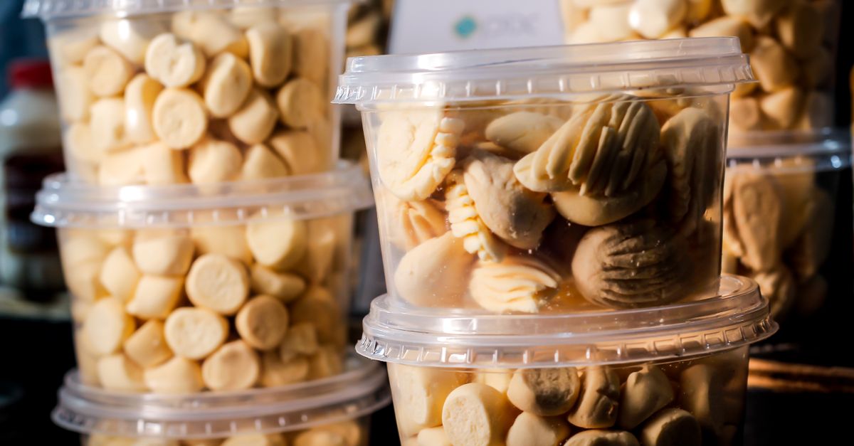 Gestapelde doorzichtige plastic bakjes gevuld met koekjes, met deksels erop en ernaast op een toonbank.