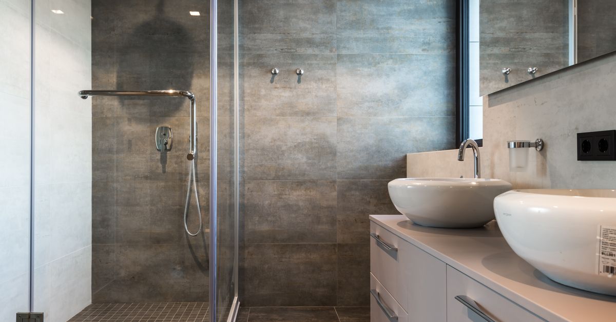 Een moderne badkamer met een glazen douchedeur en een chromen douchekop tegen een grijze tegelwand.