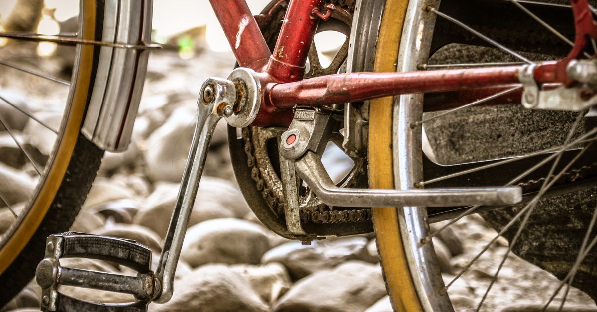 Close-up van een fietsketting en tandwiel bij het frame van een rode fiets, met kiezelstenen op de achtergrond.