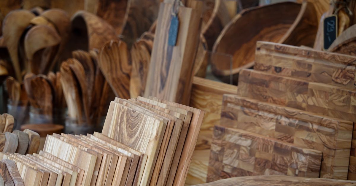 Een stapel houten snijplanken in verschillende houtsoorten en vormen uitgestald op een marktkraam.