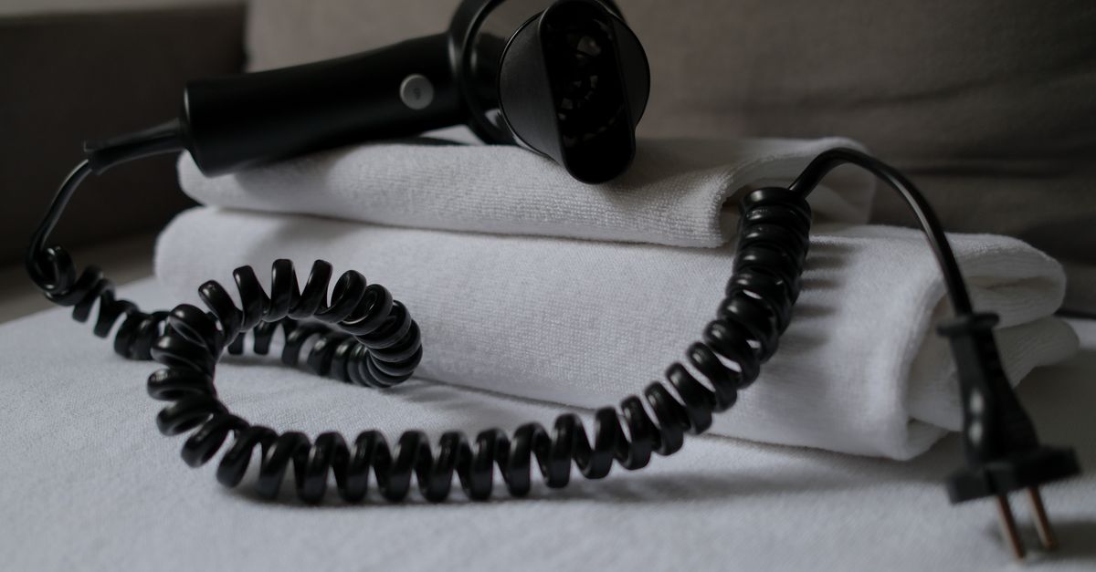 Een opgevouwen stapel witte handdoeken met een föhn met gekrulde kabel erop