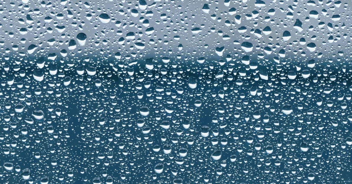 Close-up van condensdruppels op een raam met een blauwe lucht op de achtergrond.