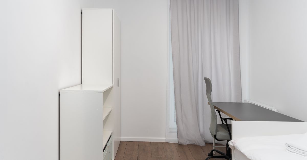 Compacte werkhoek met bureau en stoel bij het raam in een klein, licht ingerichte kamer met witte kast.