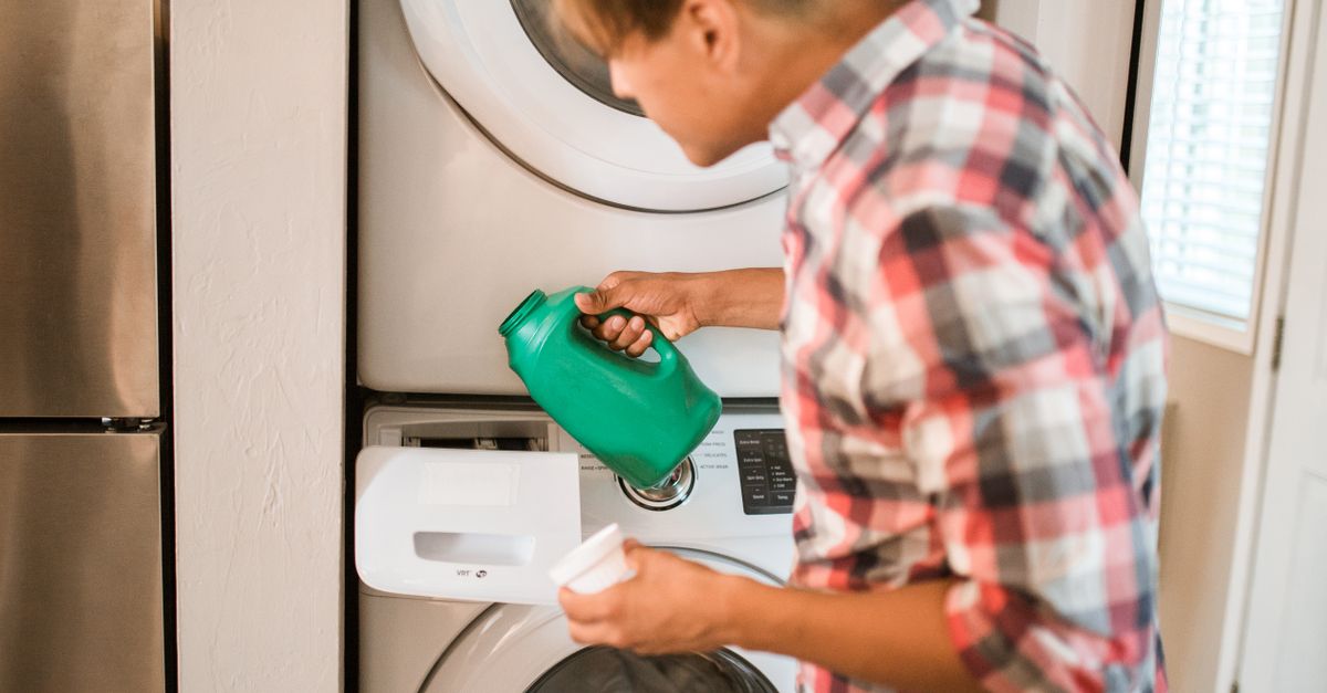 Een persoon giet groene wasmiddel uit een fles in het wasmiddelbakje van een wasmachine.