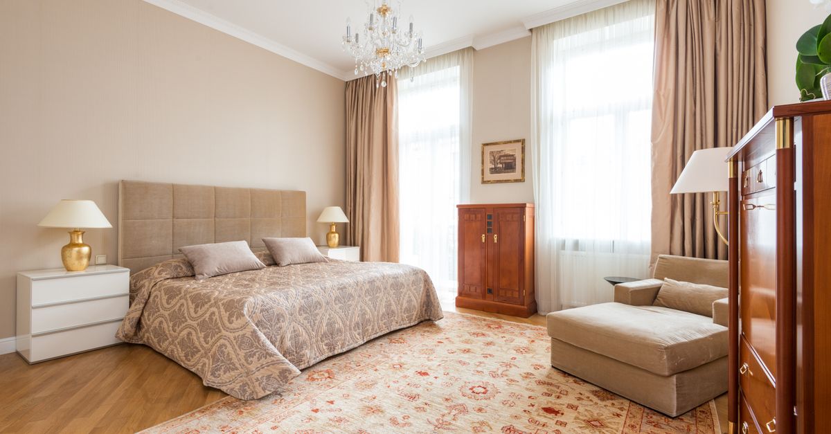 Ruime slaapkamer met een houten vloer, een tweepersoonsbed en een groot tapijt ervoor met daaromheen zichtbaar houten parket.