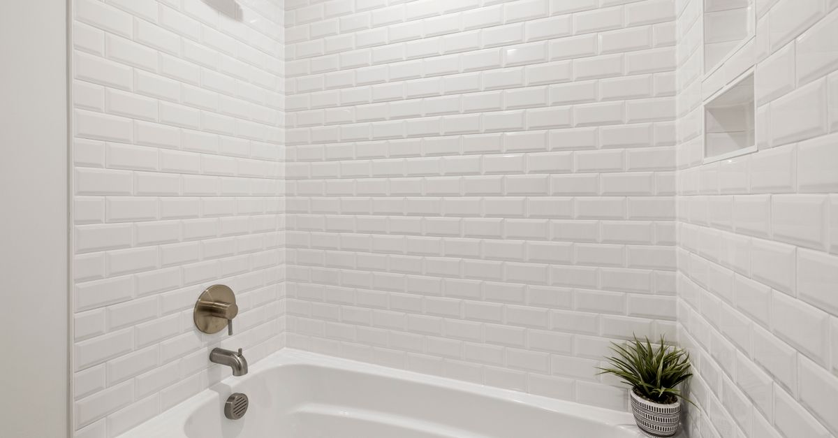 Close-up van een witte badkuip met witte betegelde wand en schoon wit voegwerk rondom de kraan.