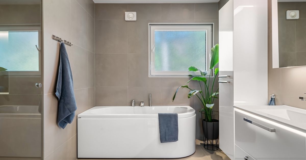Moderne badkamer met witte tegels, een ligbad en een beslagen raam dat op een kier staat voor ventilatie.