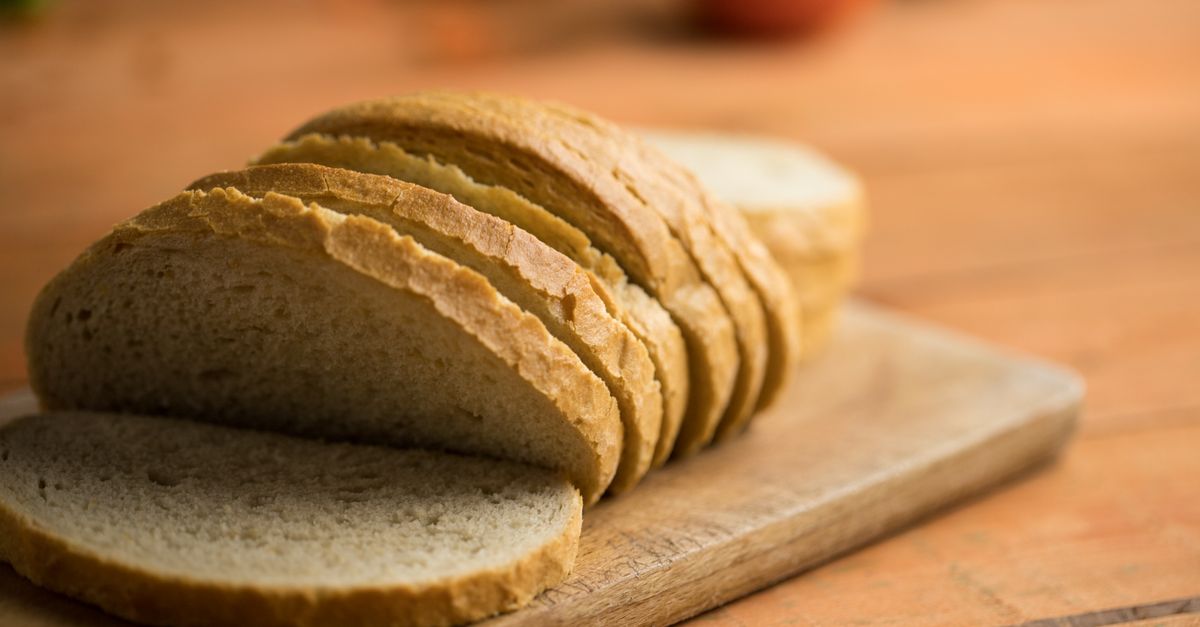 Een gesneden brood ligt op een houten snijplank op een houten tafel.