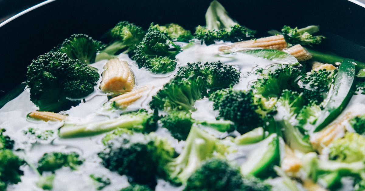 Groene groenten zoals broccoli en babymais worden geblancheerd in een pan met kokend water.