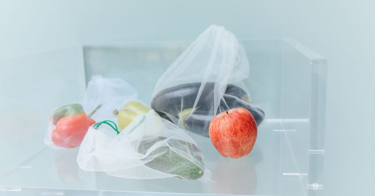 Groenten en fruit in doorzichtige netzakjes liggen op een glazen plank in de koelkast.