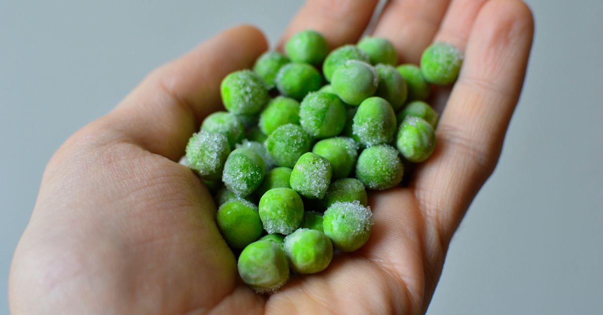 Close-up van een hand met bevroren groene erwten met een laagje ijskristallen erop.