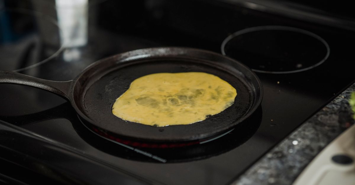 Een omelet wordt gebakken in een gietijzeren pan op een kookplaat.
