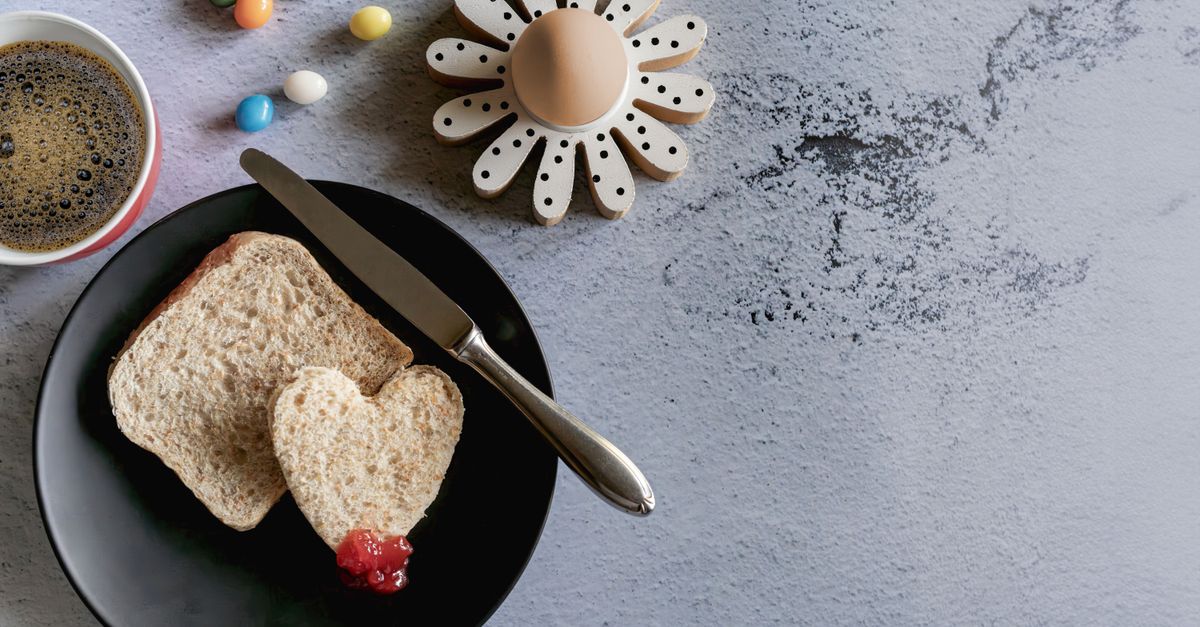 Een gepeld zachtgekookt ei in een houten eierdopje in de vorm van een bloem, naast een bord met toast en een kop koffie.
