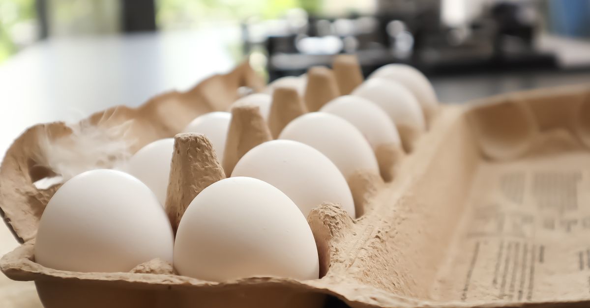 Witte eieren in een kartonnen eierdoos op het aanrecht, met een fornuis wazig op de achtergrond.