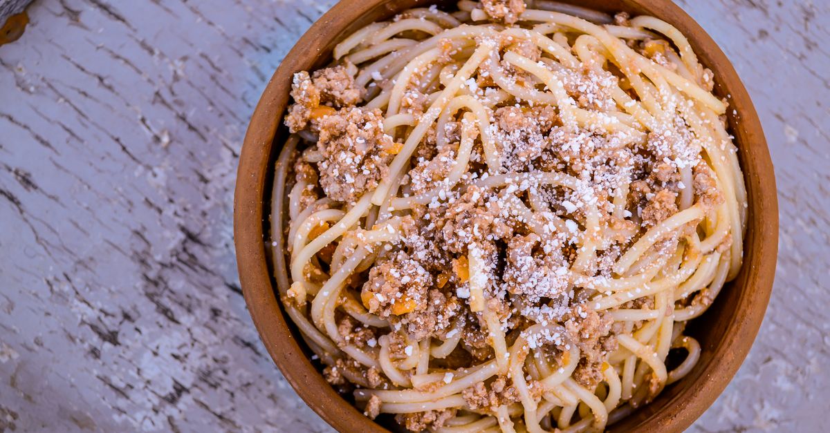 Een kom spaghetti met gehakt en saus, bestrooid met geraspte kaas, op een houten tafel.