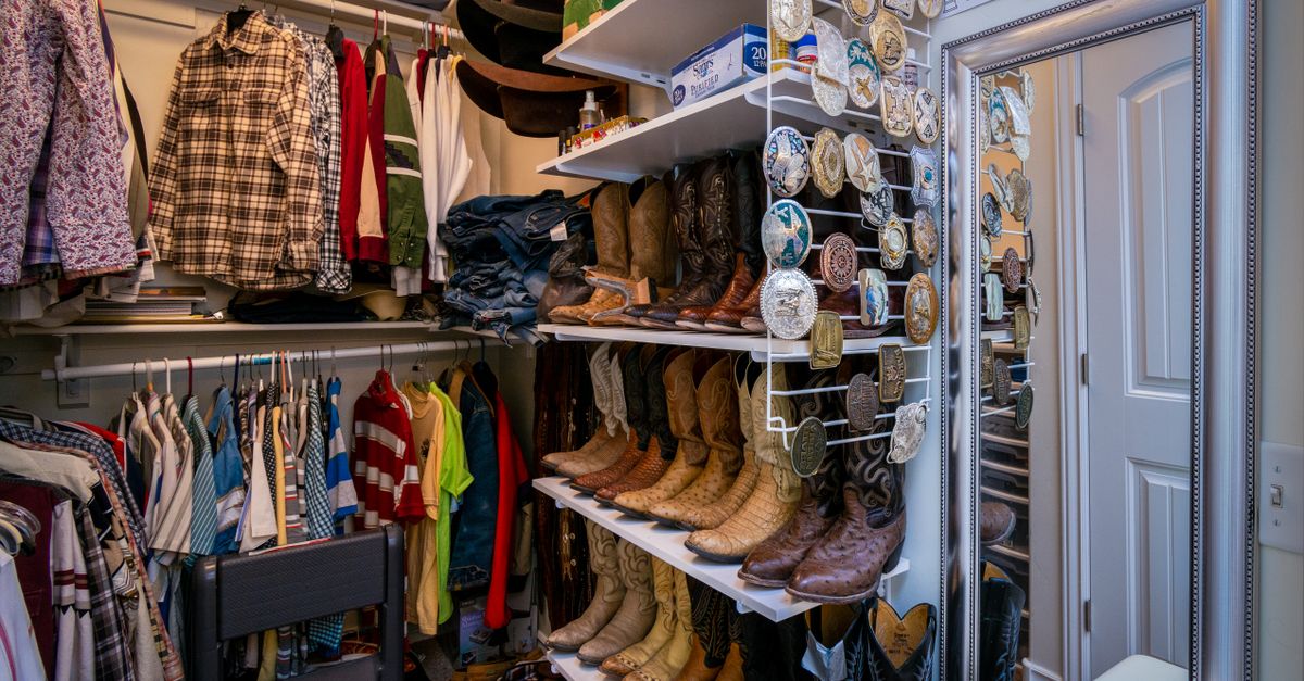 Een overzichtelijke inloopkast met opgehangen kleding, planken met opgevouwen stapels en een rek met laarzen en riemgespen.
