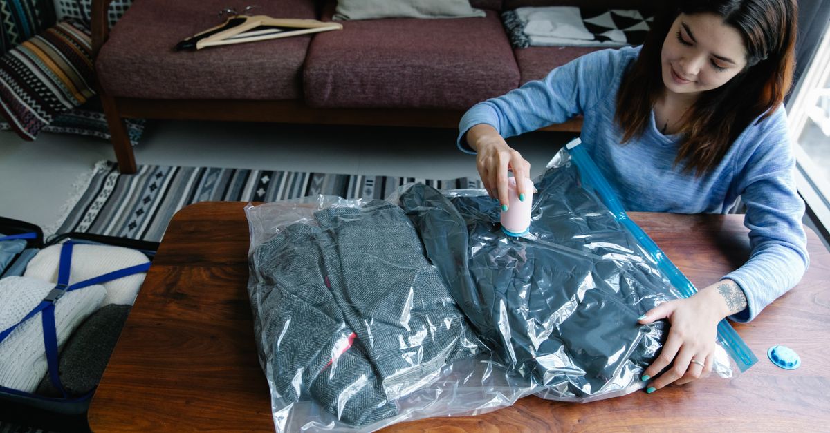 Een vrouw gebruikt een vacuümpomp om kleding in een plastic vacuümzak samen te persen op een houten tafel.