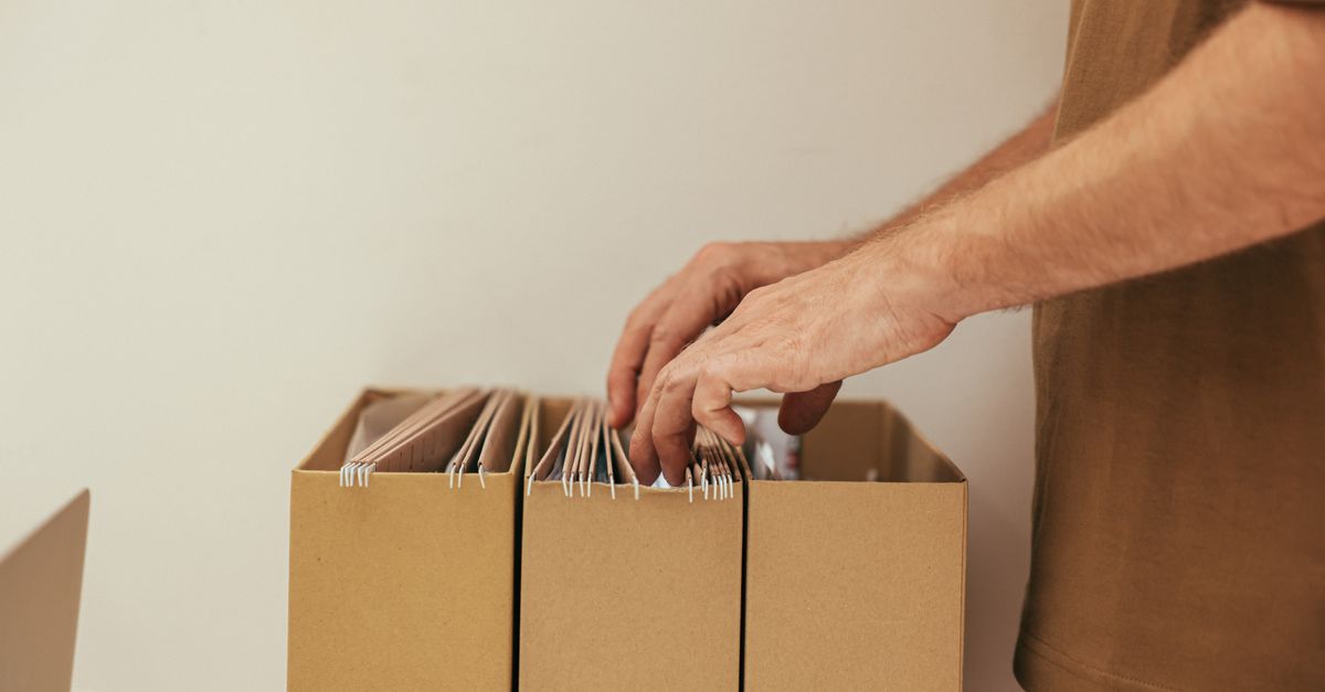 Iemand ordent kartonnen documentmappen in een opbergbox op kantoor.