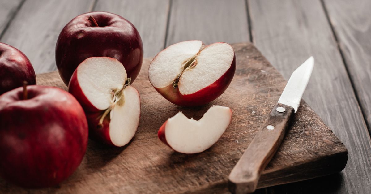Rode appels, waarvan enkele in partjes gesneden, liggen op een houten snijplank naast een mes.